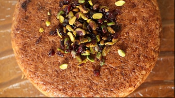 Sobre uma superfície marrom com relevos está o tah-chin, prato à base de arroz e frango, em forma de círculo - com aparência de um bolo em tom caramelo. Por cima, há pedaços de pistache e cranberry. Foto: FELIPE RAU